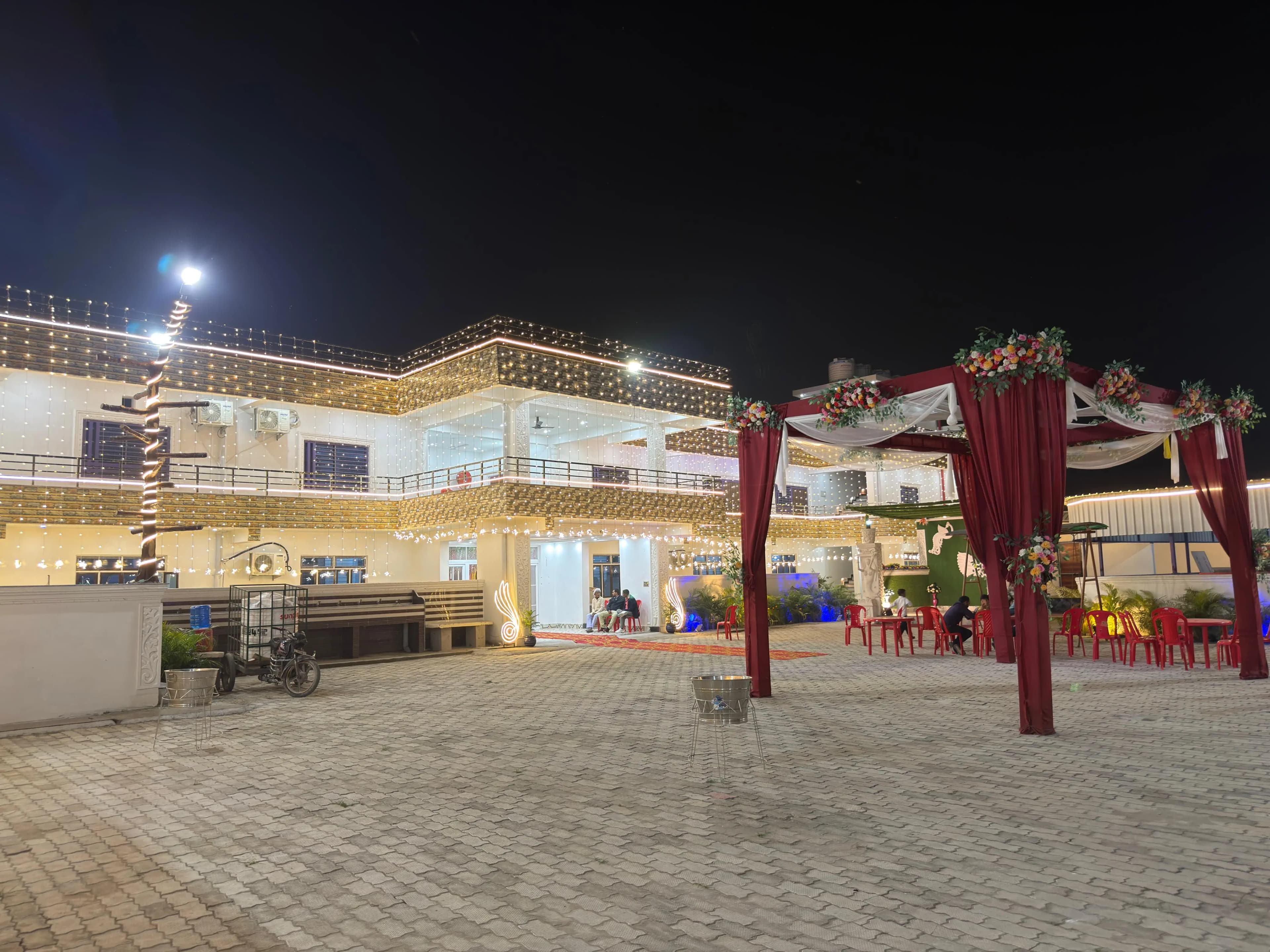 The full Janki Resort property lit with string lights at night, with a maroon draped mandap and guest seating across the paved courtyard