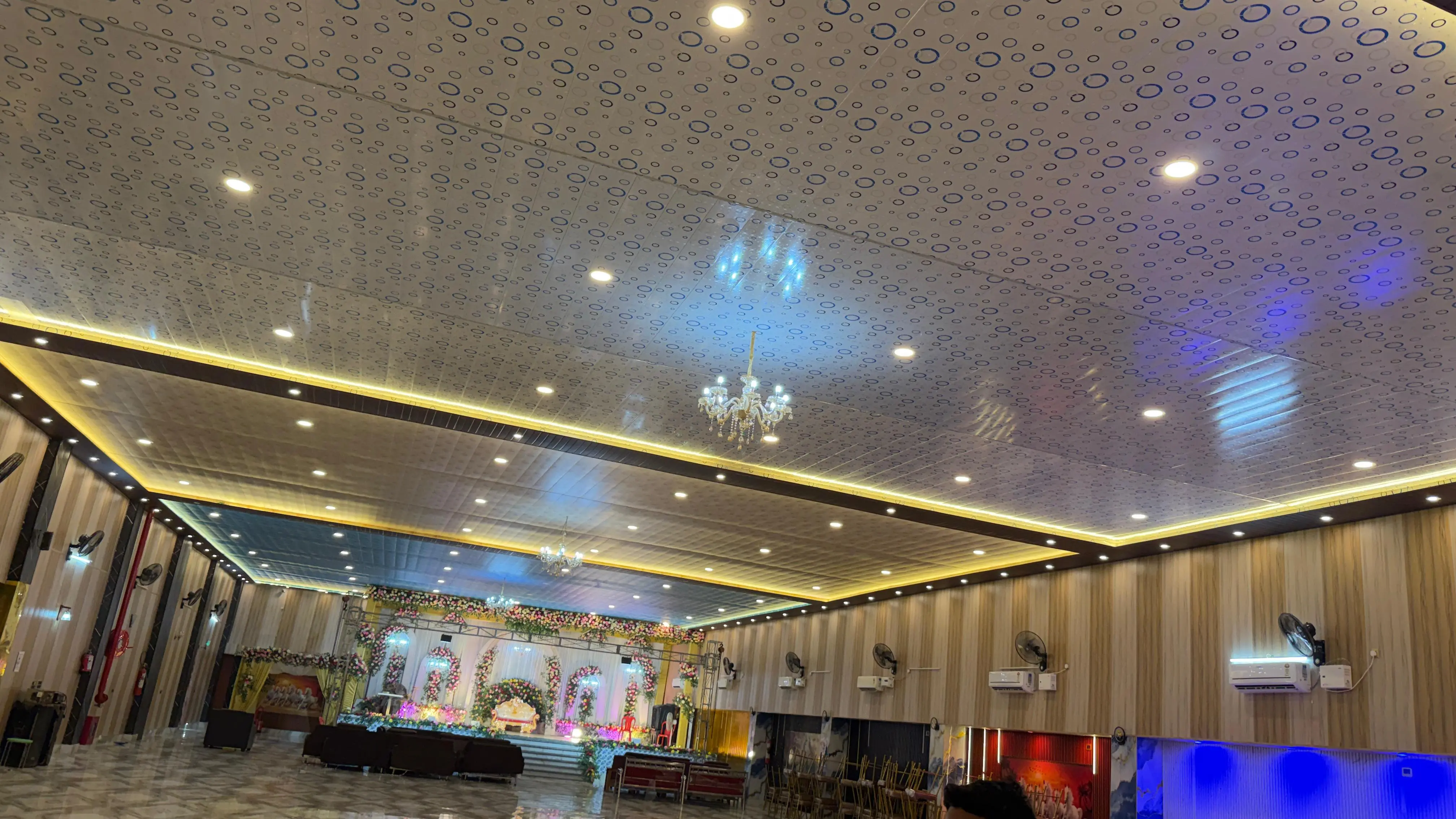 The hall's patterned ceiling with chandeliers and gold cove lighting above the open floor