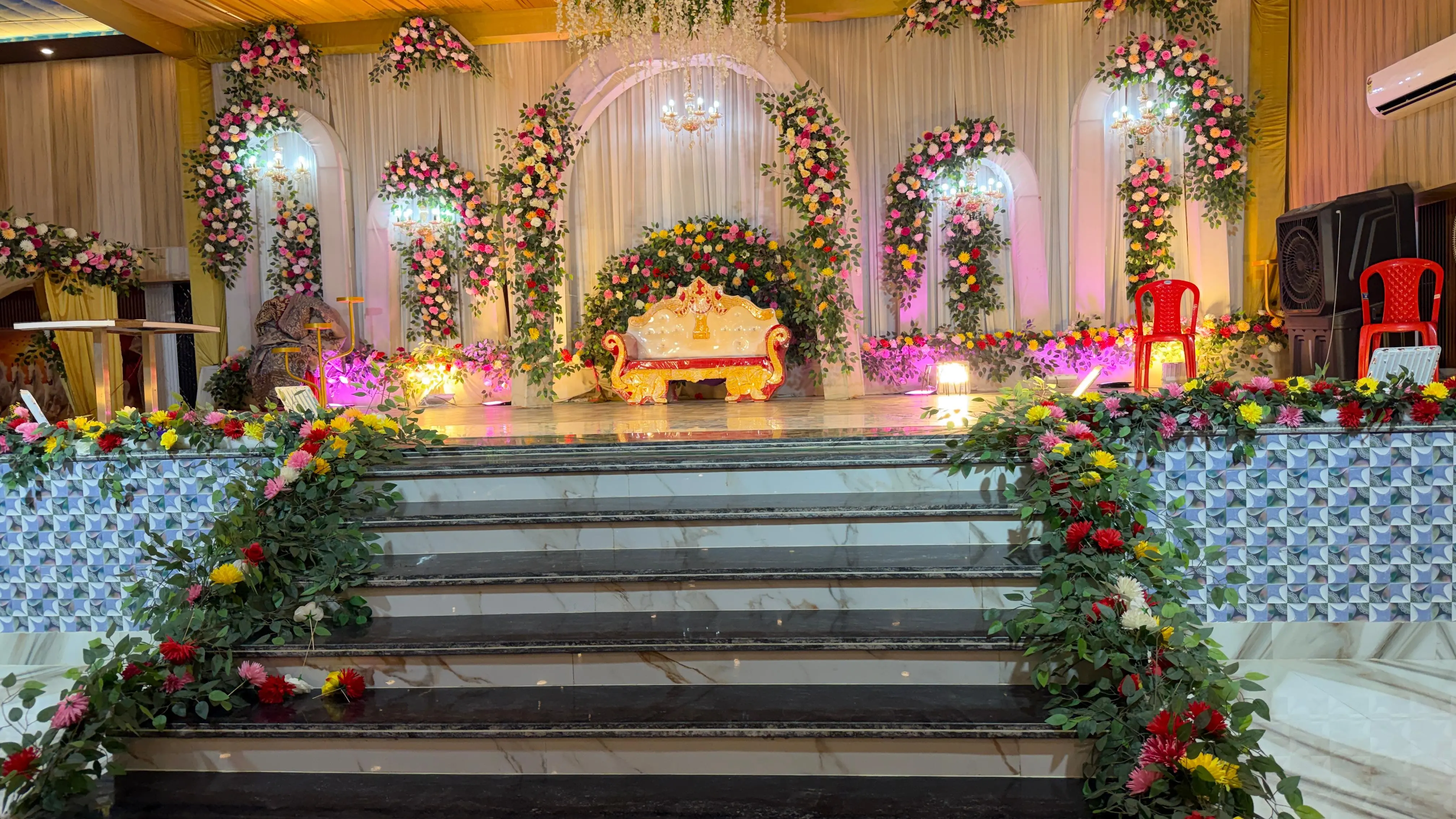 Close view of the decorated stage — a gilded sofa beneath a flower arch, with garlanded steps leading up
