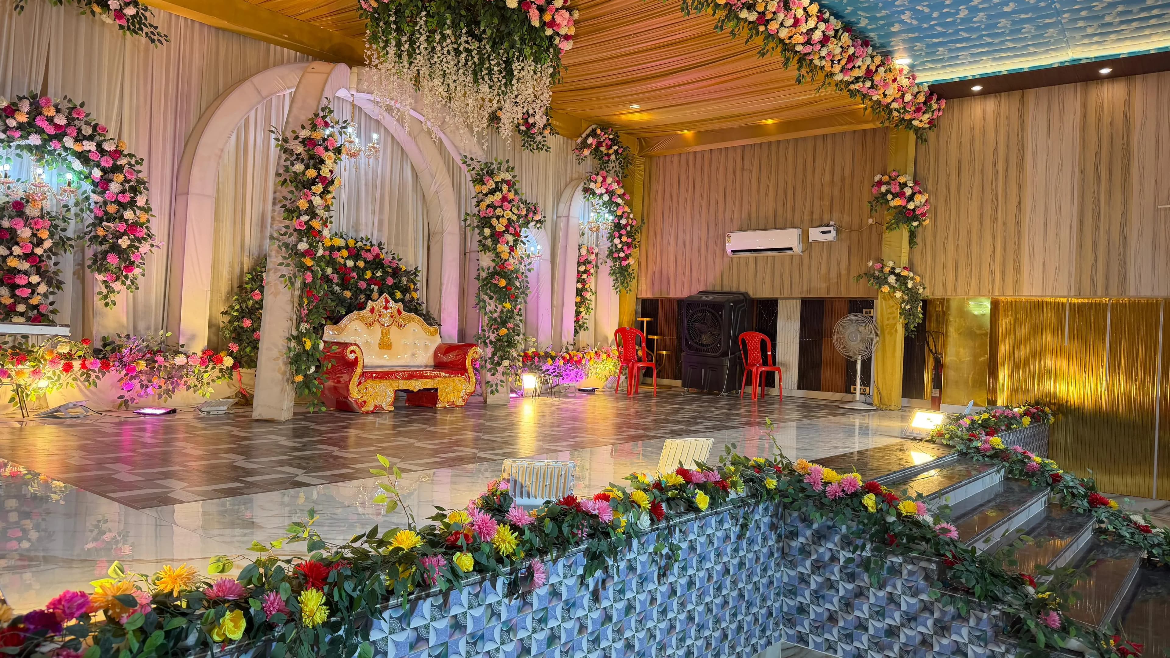 The hall seen from one side, floral installations along the wall and the stage lit at the far end
