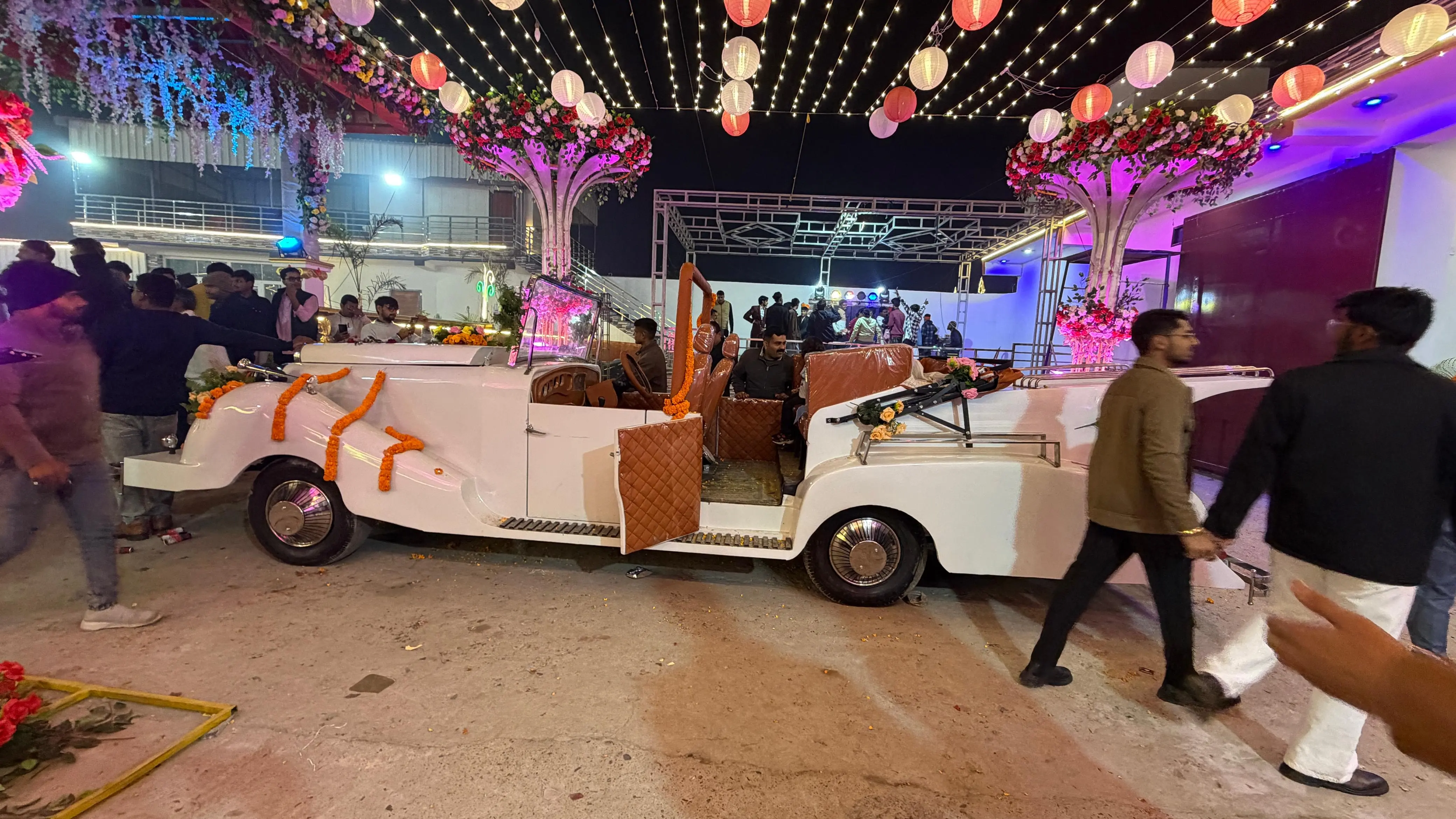 A decorated vintage wedding car in the lantern-lit forecourt, with guests alongside