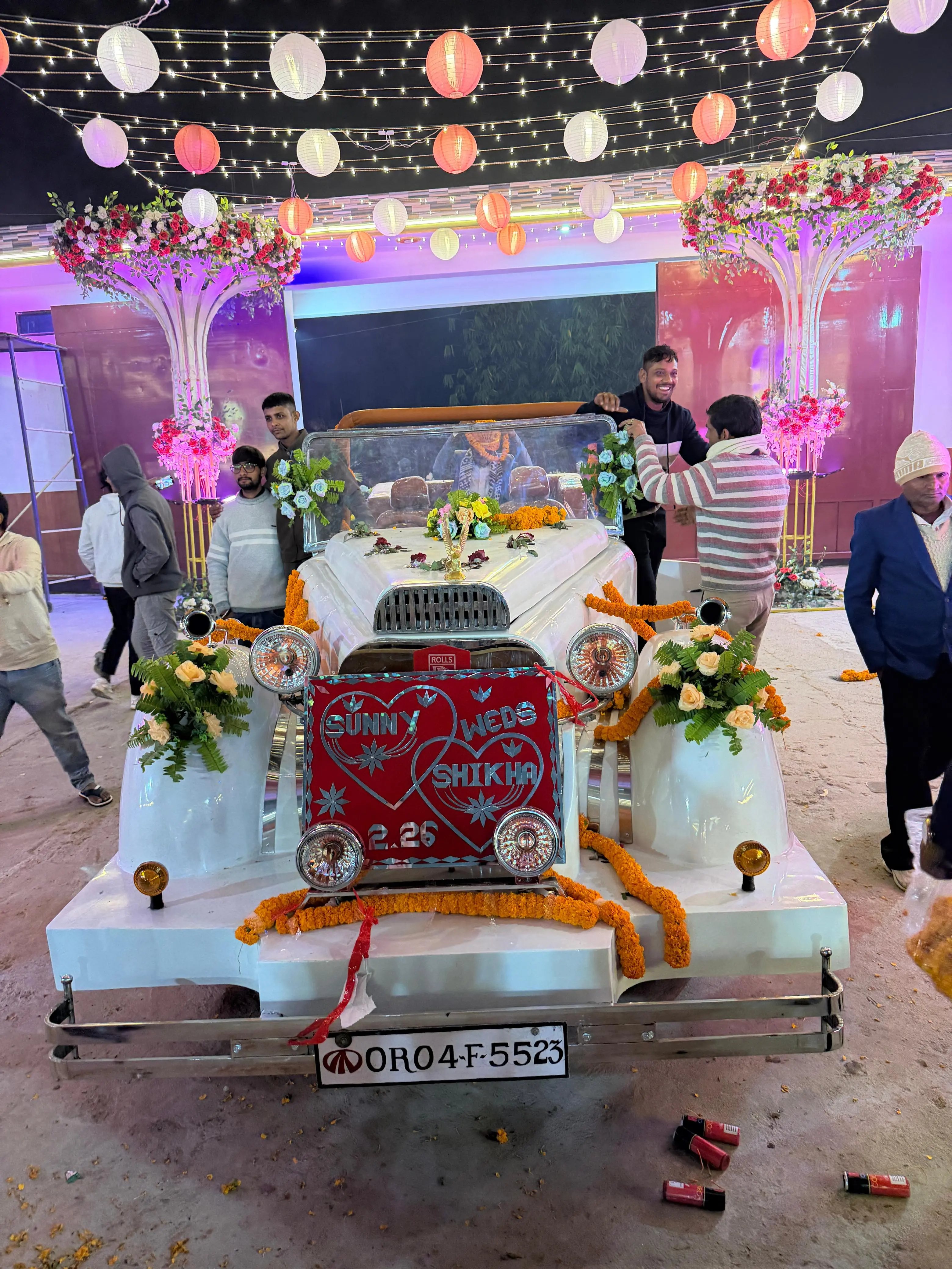 The wedding car dressed with marigold garlands and roses, parked beneath the lantern canopy
