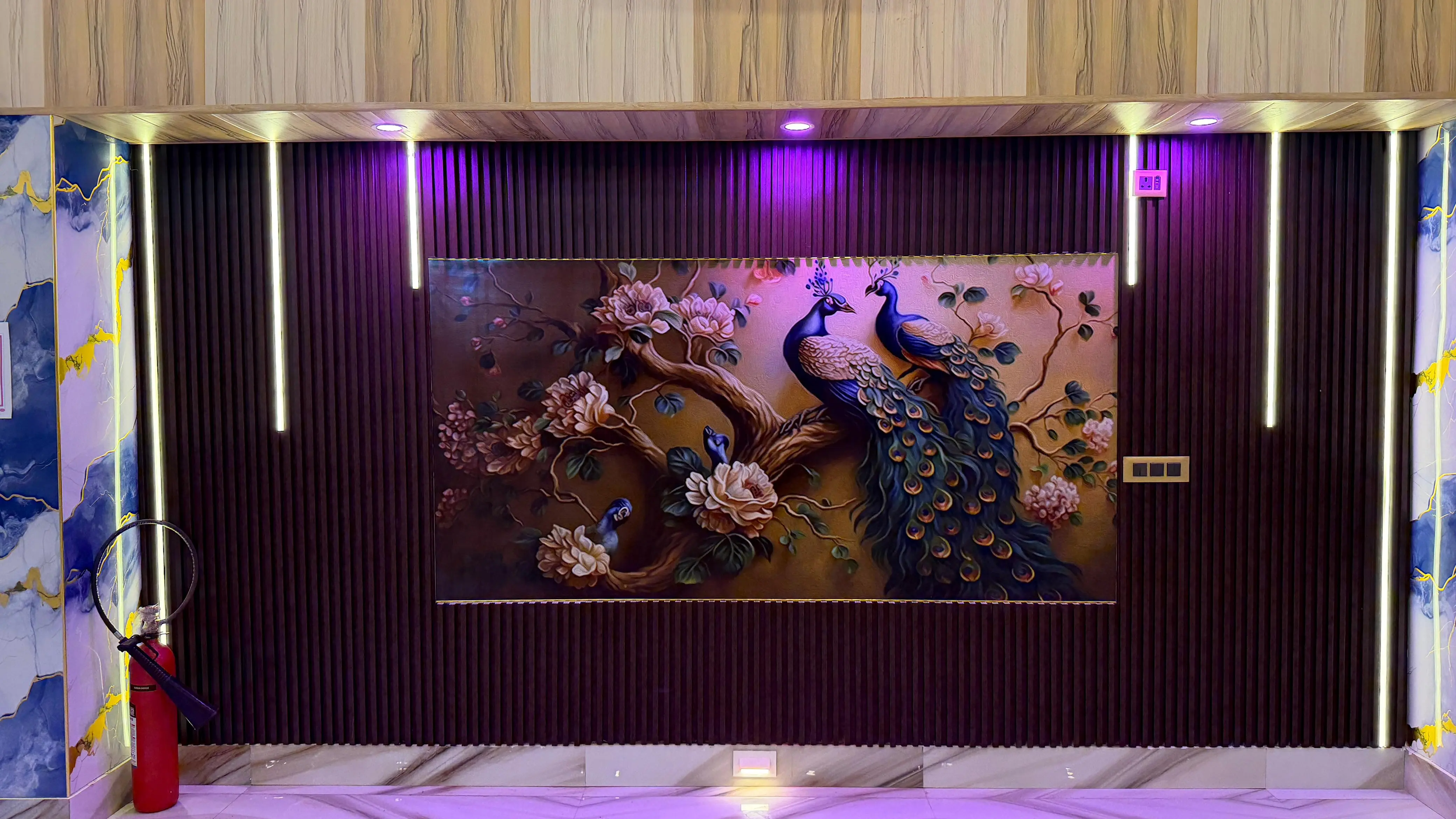 A large peacock mural lit against dark fluted panelling, flanked by marble-effect columns